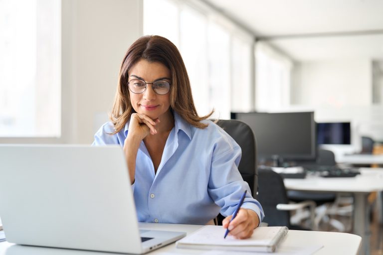 Busy middle aged business woman worker working on laptop in office writing note.